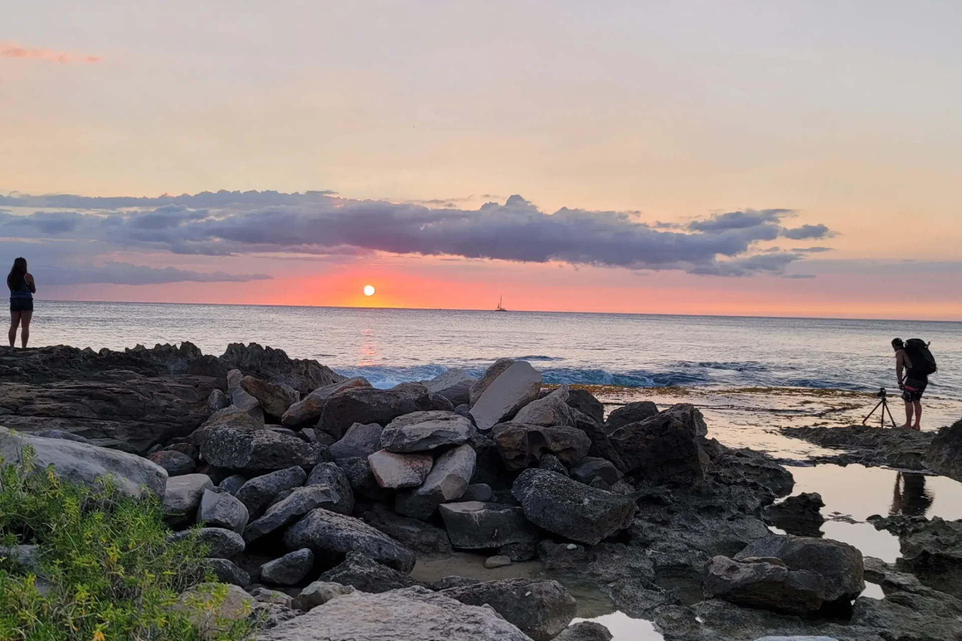 A sunset over the ocean with rocks in front of it.