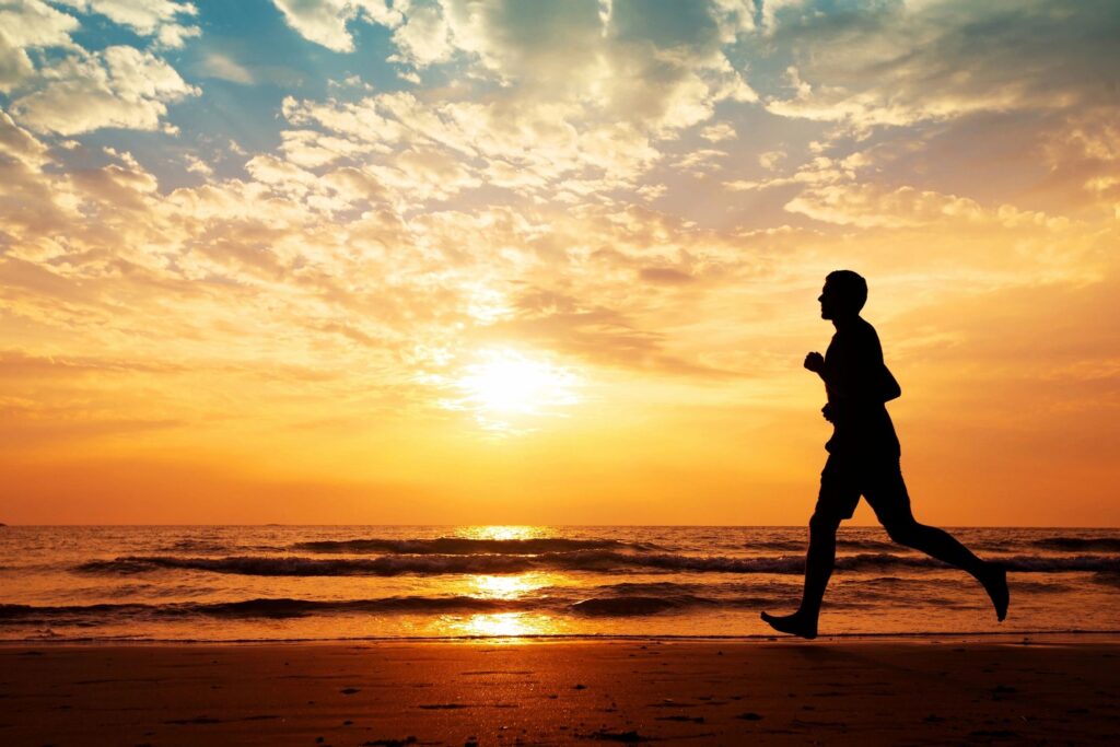 Man jogging on beach at sunset.