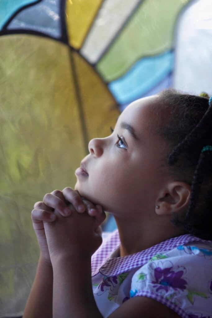 Girl praying by stained glass window.