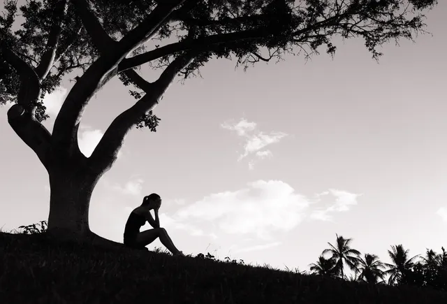 Silhouette of sad woman under tree.