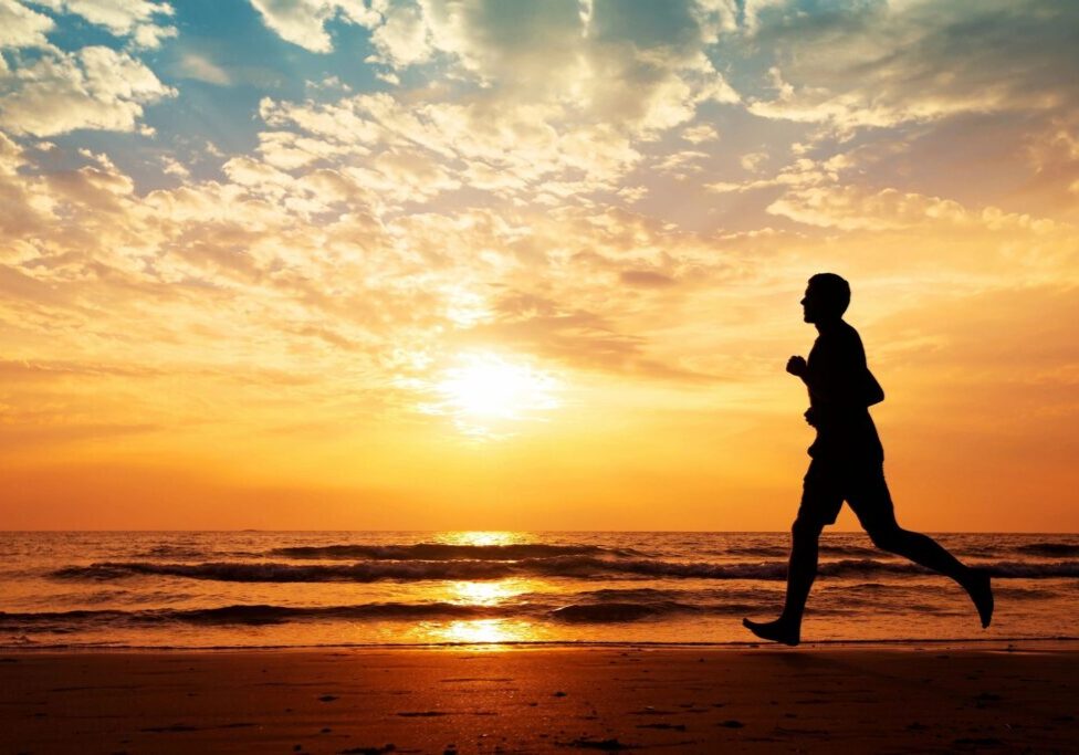 Man jogging on beach at sunset.