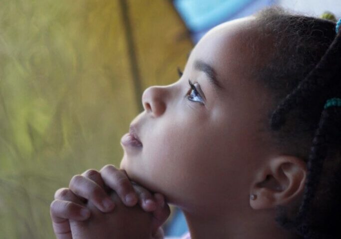 Girl praying by stained glass window.